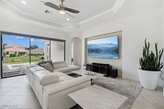 living room with ornamental molding, light tile patterned flooring, a tray ceiling, and ceiling fan