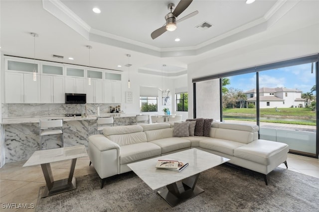 tiled living room featuring crown molding, a raised ceiling, and ceiling fan