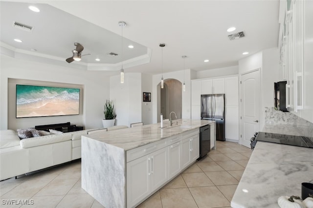 kitchen with an island with sink, black appliances, decorative light fixtures, white cabinets, and light stone counters