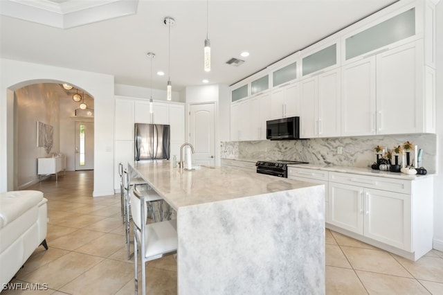 kitchen featuring white cabinetry, stainless steel appliances, decorative light fixtures, and an island with sink