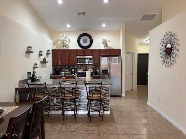 kitchen featuring kitchen peninsula, a breakfast bar area, stainless steel appliances, decorative backsplash, and light tile patterned floors