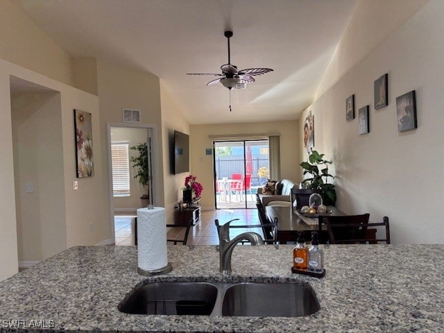 kitchen with sink, ceiling fan, lofted ceiling, light stone counters, and light tile patterned floors