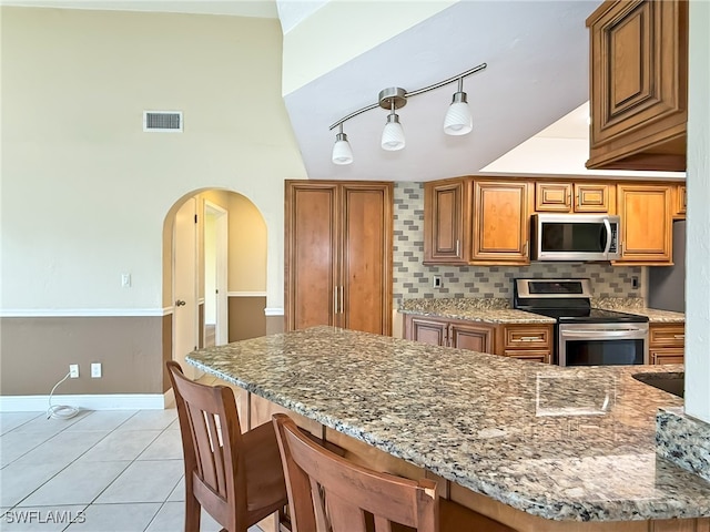 kitchen featuring lofted ceiling, backsplash, a kitchen breakfast bar, light stone countertops, and stainless steel appliances