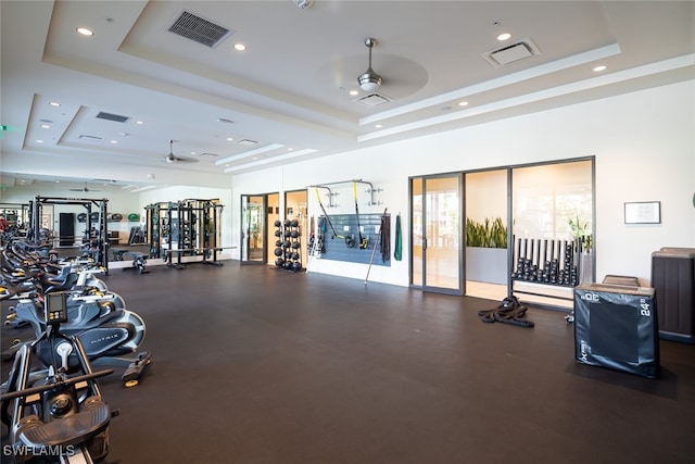 gym with a tray ceiling and ceiling fan