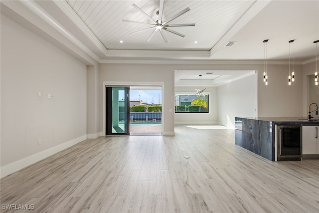 unfurnished living room featuring light wood-type flooring, a tray ceiling, beverage cooler, and ornamental molding