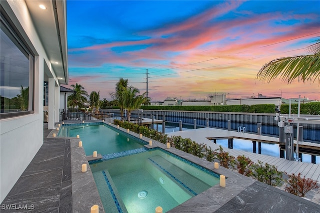 pool at dusk with an in ground hot tub and a water view