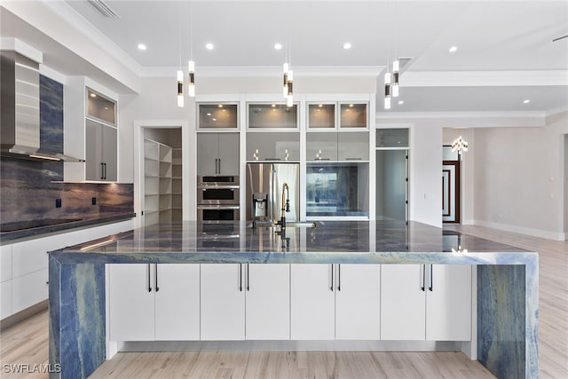 kitchen featuring a large island, hanging light fixtures, wall chimney range hood, and light hardwood / wood-style floors