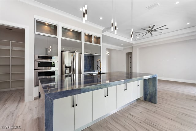 kitchen with pendant lighting, a large island with sink, sink, light hardwood / wood-style flooring, and appliances with stainless steel finishes