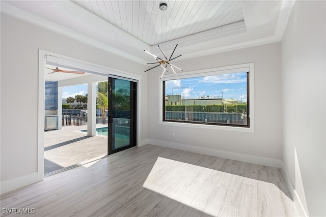 spare room with a raised ceiling, light hardwood / wood-style floors, and a notable chandelier