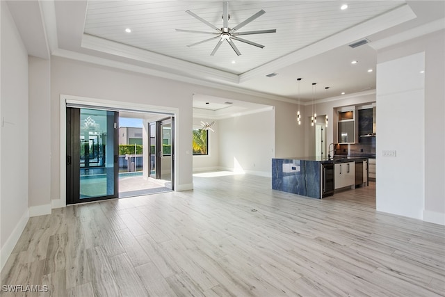 unfurnished living room featuring a tray ceiling, ornamental molding, ceiling fan with notable chandelier, and light wood-type flooring