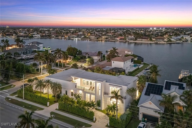 aerial view at dusk with a water view and a residential view