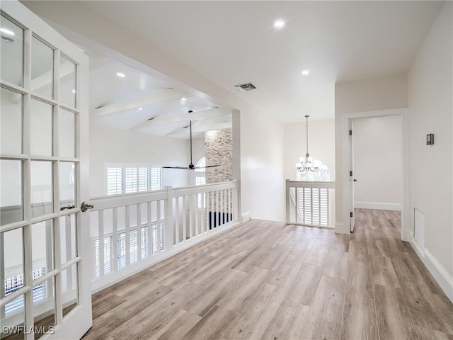 empty room with lofted ceiling with beams, ceiling fan with notable chandelier, and light wood-type flooring