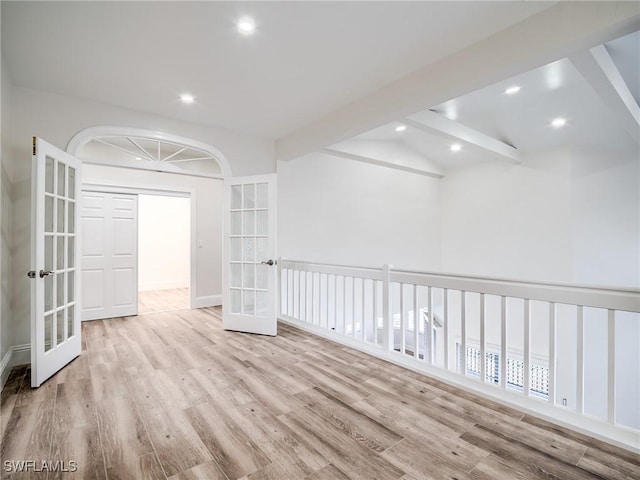 empty room with french doors, light hardwood / wood-style floors, and vaulted ceiling with beams