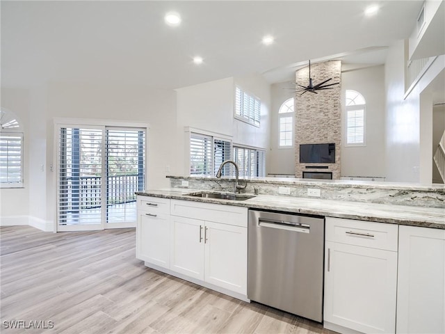 kitchen featuring a wealth of natural light, dishwasher, sink, white cabinets, and light stone countertops