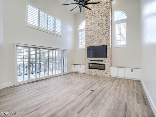 unfurnished living room featuring a high ceiling, ceiling fan, a stone fireplace, and light wood-type flooring