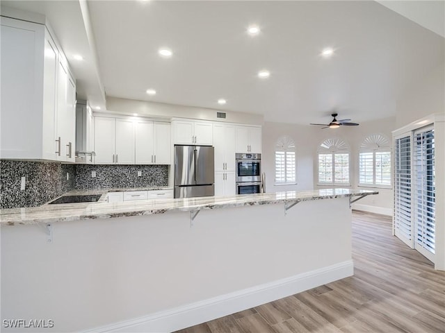 kitchen featuring stainless steel appliances, white cabinetry, light stone counters, and kitchen peninsula