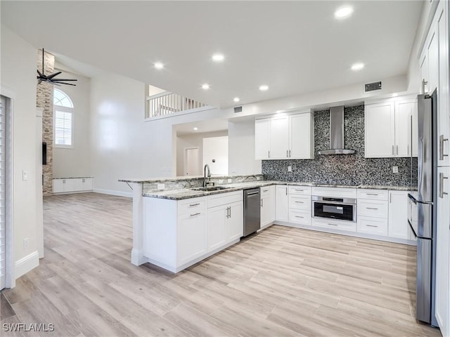 kitchen featuring white cabinetry, stainless steel appliances, light stone counters, kitchen peninsula, and wall chimney exhaust hood