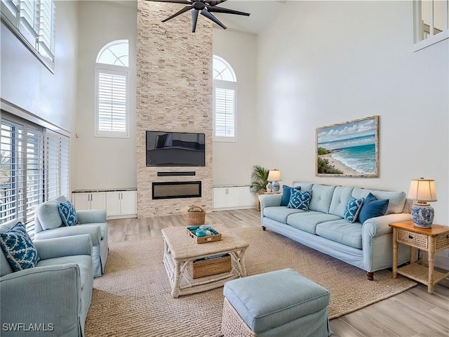 living room featuring ceiling fan, a large fireplace, light hardwood / wood-style floors, and a towering ceiling