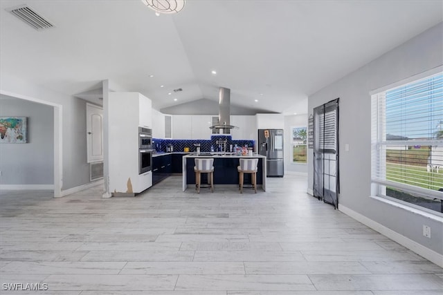 kitchen featuring lofted ceiling, a breakfast bar area, stainless steel appliances, a center island with sink, and white cabinetry