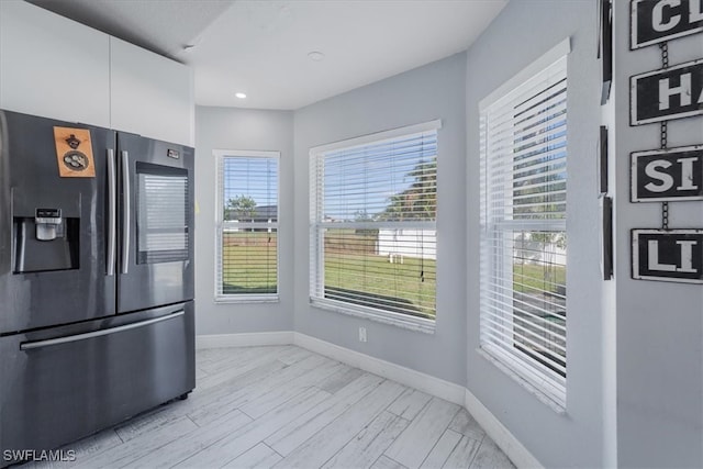 kitchen with stainless steel fridge, light hardwood / wood-style flooring, white cabinetry, and plenty of natural light