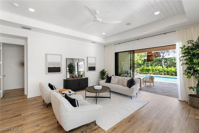 living room featuring ceiling fan, a raised ceiling, and light hardwood / wood-style flooring