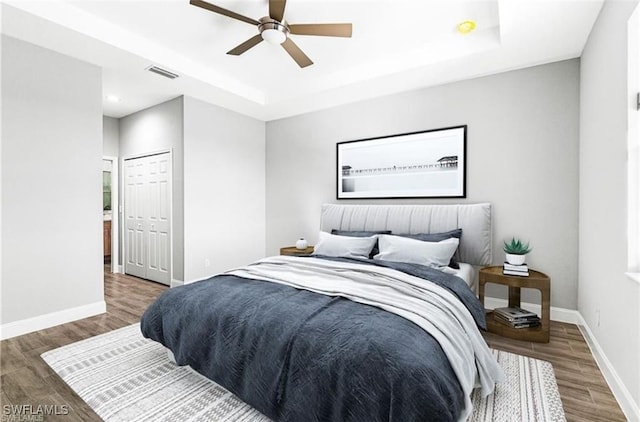 bedroom with a closet, a tray ceiling, wood-type flooring, and ceiling fan