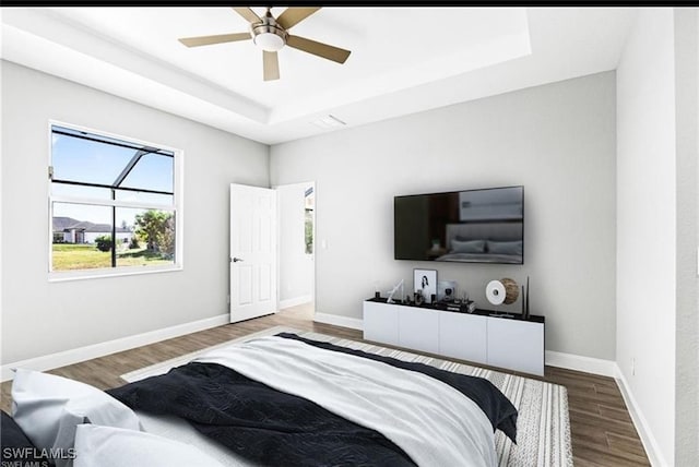 bedroom with wood-type flooring, ceiling fan, and a raised ceiling