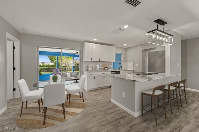 kitchen featuring light stone countertops, hanging light fixtures, light hardwood / wood-style flooring, and white cabinets