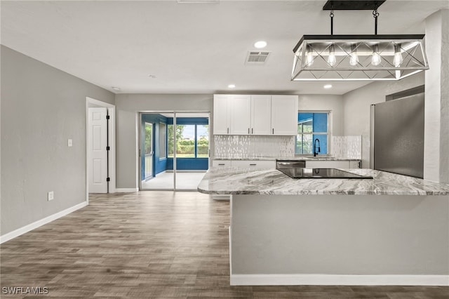 kitchen with a wealth of natural light, appliances with stainless steel finishes, white cabinetry, and light stone countertops