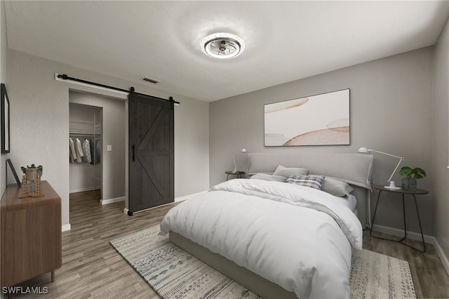 bedroom featuring a closet, a walk in closet, a barn door, and hardwood / wood-style floors