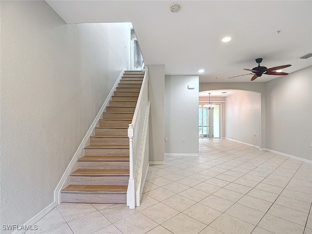 stairway with tile patterned floors and ceiling fan with notable chandelier