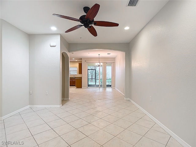 tiled empty room featuring ceiling fan with notable chandelier