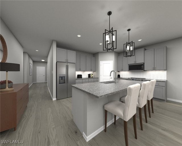 kitchen featuring gray cabinetry, stainless steel appliances, a notable chandelier, an island with sink, and light wood-type flooring