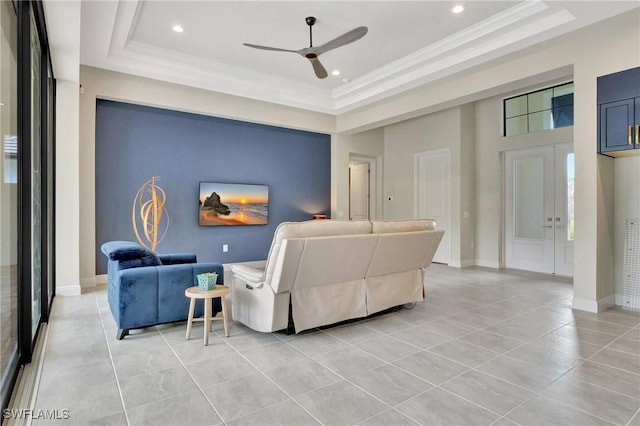 living room with light tile patterned floors, ceiling fan, a towering ceiling, ornamental molding, and a raised ceiling