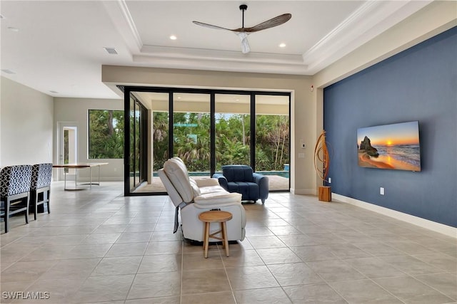 tiled living room with a raised ceiling, ornamental molding, and ceiling fan