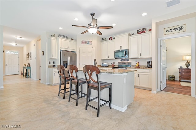 kitchen with light stone counters, a center island with sink, appliances with stainless steel finishes, a kitchen breakfast bar, and white cabinets