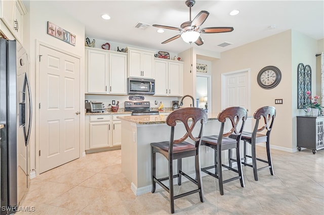 kitchen featuring stainless steel appliances, white cabinetry, light stone countertops, a breakfast bar area, and a kitchen island with sink