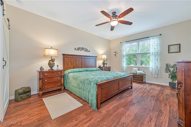 bedroom featuring dark hardwood / wood-style flooring, a barn door, and ceiling fan