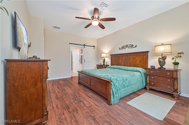 bedroom with a barn door, ceiling fan, connected bathroom, and dark hardwood / wood-style flooring