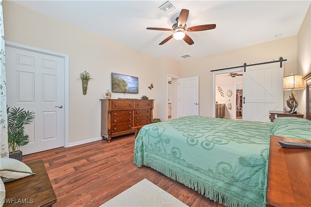 bedroom with connected bathroom, dark hardwood / wood-style flooring, a barn door, and ceiling fan