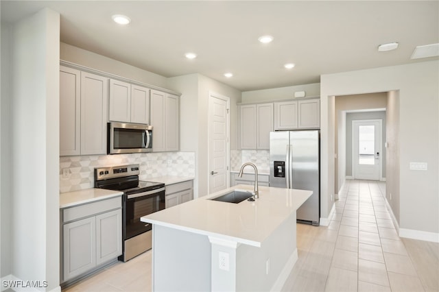 kitchen with stainless steel appliances, gray cabinetry, an island with sink, and sink