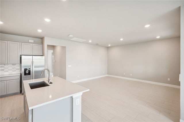 kitchen with backsplash, gray cabinets, sink, and a kitchen island with sink