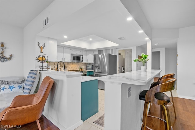 kitchen with appliances with stainless steel finishes, kitchen peninsula, white cabinetry, and light hardwood / wood-style floors