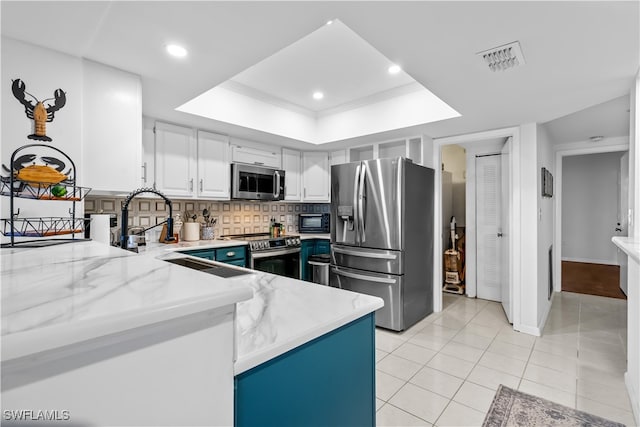 kitchen with white cabinets, tasteful backsplash, a raised ceiling, light tile patterned floors, and stainless steel appliances