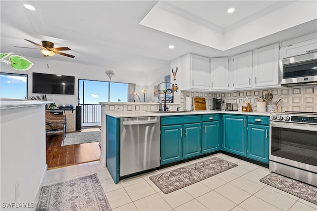 kitchen with kitchen peninsula, ornamental molding, white cabinets, appliances with stainless steel finishes, and tasteful backsplash