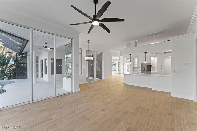 unfurnished living room featuring sink, light wood-type flooring, ceiling fan, and ornamental molding