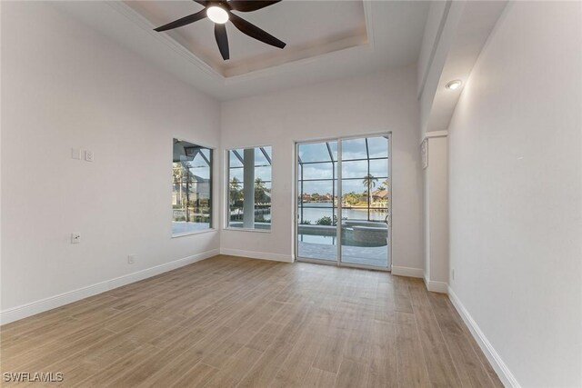 spare room featuring ceiling fan, light hardwood / wood-style flooring, a water view, and a tray ceiling