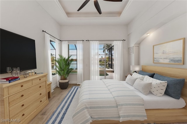 bedroom with light hardwood / wood-style floors, ceiling fan, and a raised ceiling