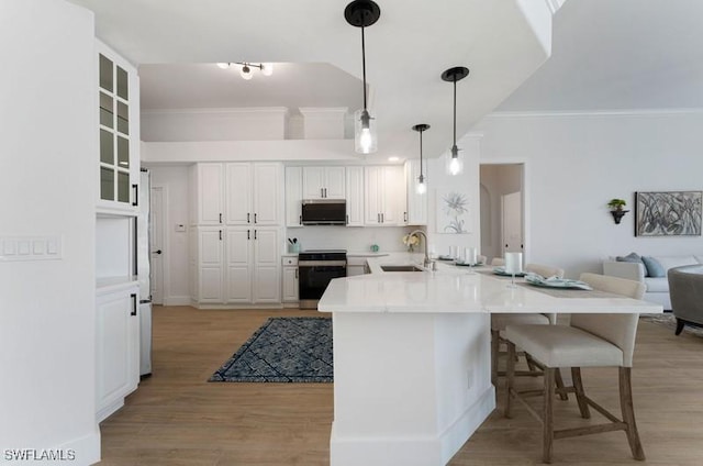 kitchen featuring a breakfast bar area, stainless steel microwave, stove, a sink, and a peninsula