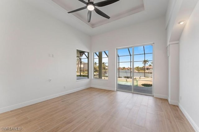 unfurnished room with light wood-style flooring, a high ceiling, a ceiling fan, baseboards, and a raised ceiling